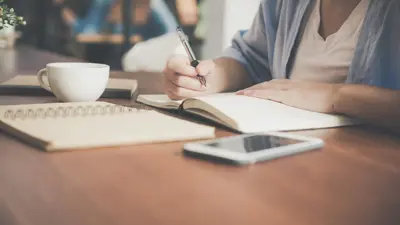 Person writing in notebook with tablet nearby